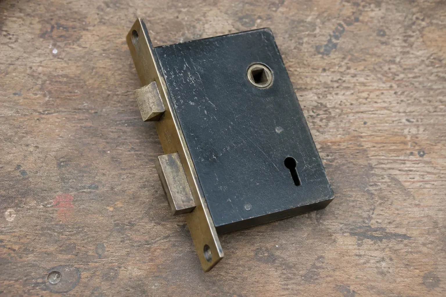 Closed mortise lock case with spindle opening, keyhole, latch and deadbolt on a wooden workbench. — Vintage Mortise Lock Service, Haldimand County