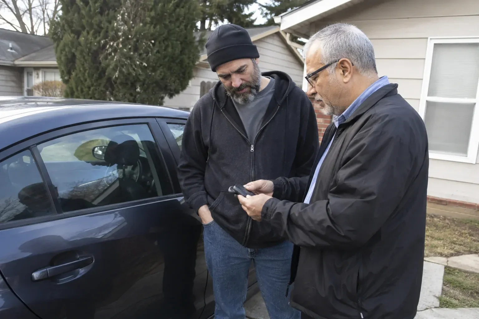 Two adults discussing a key fob beside a parked car. — Car Lockout Service, Haldimand County